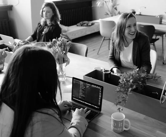 Three women at their workplace. One of them is laughing.