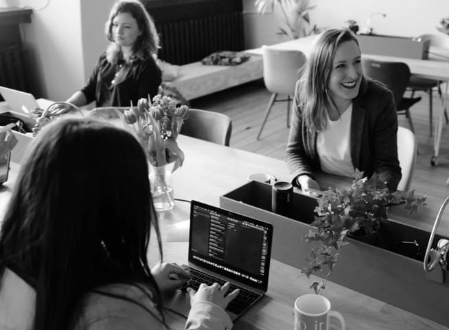 Three women at their workplace. One of them is laughing.